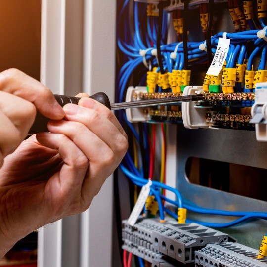 Mâinile unui bărbat cu şurubelnită umblând la fire şi cabluri etichetate