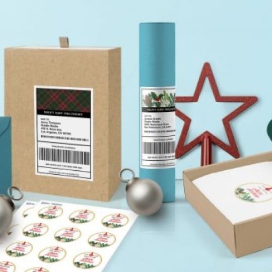 Diferite ambalaje pentru cadouri cu etichete de adresă și autocolante rotunde de Crăciun lipite, în fundal decorațiuni pentru brad și o stea roșie decorativă, pe un fundal albastru deschis.