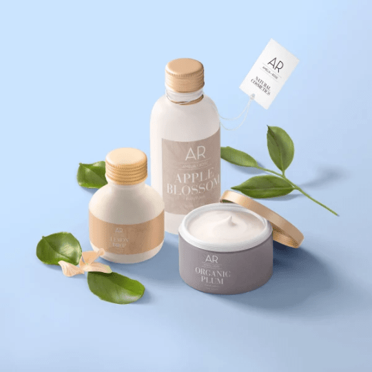Un set de trei produse cosmetice naturale Amelia Rose pe un fundal albastru deschis. Setul include două sticle și un borcan deschis cu cremă, denumite "Lemon Drop", "Apple Blossom" și "Organic Plum", înconjurate de frunze verzi.