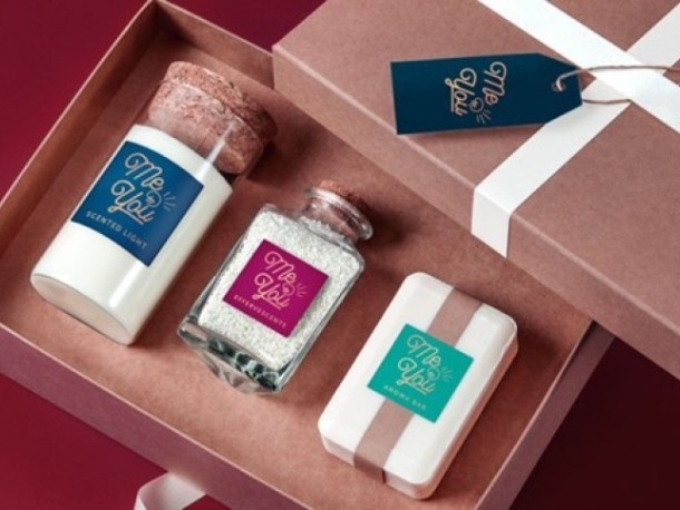 Un set cadou deschis într-o cutie, care conține trei produse cosmetice cu etichete "Me & You": o lumânare parfumată, săruri de baie într-un borcan și un săpun solid.