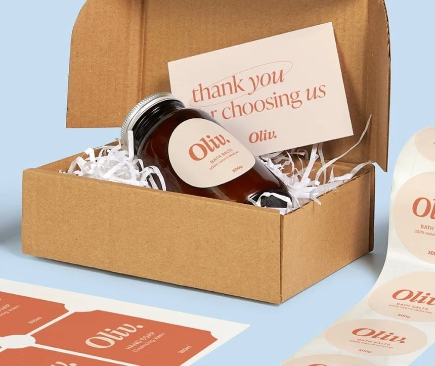 Elegancko zapakowany produkt w kartonowym pudełku. W środku, na białym wypełniaczu, leży brązowa butelka z etykietą "Oli
