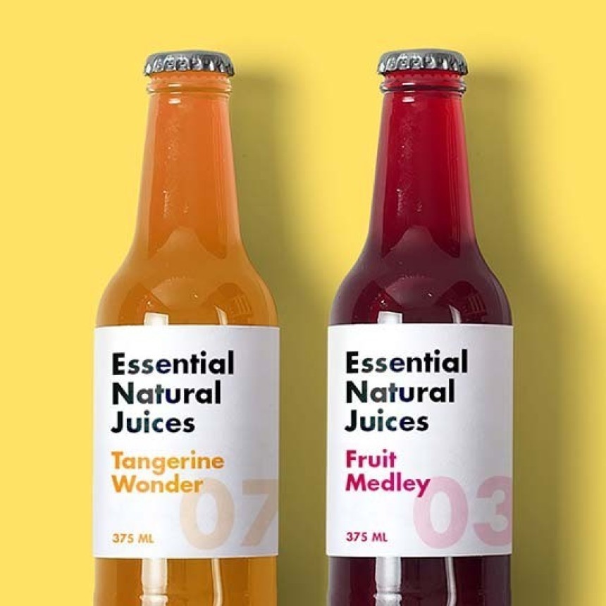 Două sticle de suc din sticlă, marca "Essential Natural Juices", așezate una lângă cealaltă pe un fundal galben deschis. Sticla din stânga, cu suc portocaliu, are o etichetă cu textul "Tangerine Wonder 07". Sticla din dreapta, cu suc roșu închis, are eticheta "Fruit Medley 03".