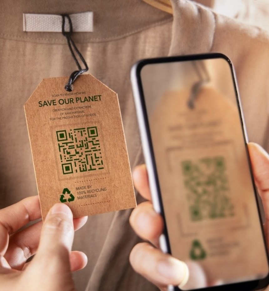 O persoană scanează cu smartphone-ul un cod QR de pe o etichetă ecologică de îmbrăcăminte cu textul "Save Our Planet" și simbolul de reciclare. Telefonul afișează informațiile scanate, demonstrând utilizarea codurilor 2D pentru a oferi date suplimentare despre produs.
