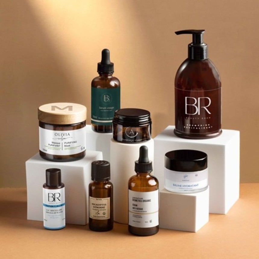 O colecție de diverse produse cosmetice organice în sticle și borcane de sticlă de culoare închisă, aranjate elegant pe piedestale albe.