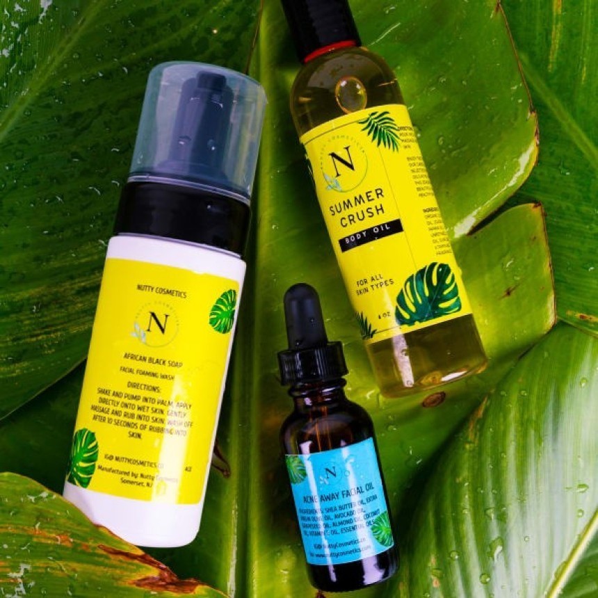 Trei produse de îngrijire a pielii marca "Nutty Cosmetics" așezate pe o frunză verde, mare. Setul include: o spumă de curățare facială, un ulei de corp "Summer Crush" și un ulei facial într-o sticlă cu pipetă.