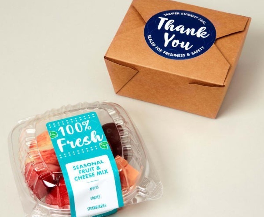 O cutie pentru take-away cu salată de fructe, având o etichetă albastră "100% Fresh", și o cutie de carton cu o etichetă rotundă "Thank You" care servește drept sigiliu de garanție.