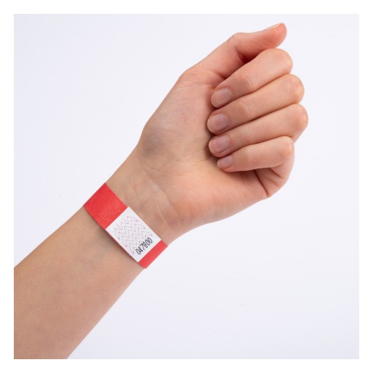 O mână care poartă o brățară roșie cu o etichetă albă care are modele zigzag și numere imprimate pe ea.