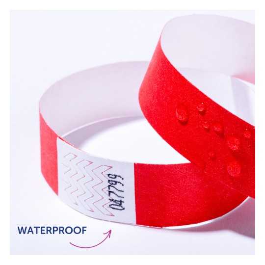 Imaginea arată o brățară roșie impermeabilă cu picături de apă pe ea. Există modele în zigzag și text pe o bandă albă a brățării.