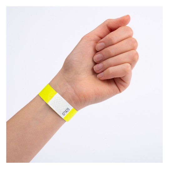 Această imagine arată o mână care poartă o brățară galbenă cu o secțiune albă ce are un model în zigzag și un număr pe ea.