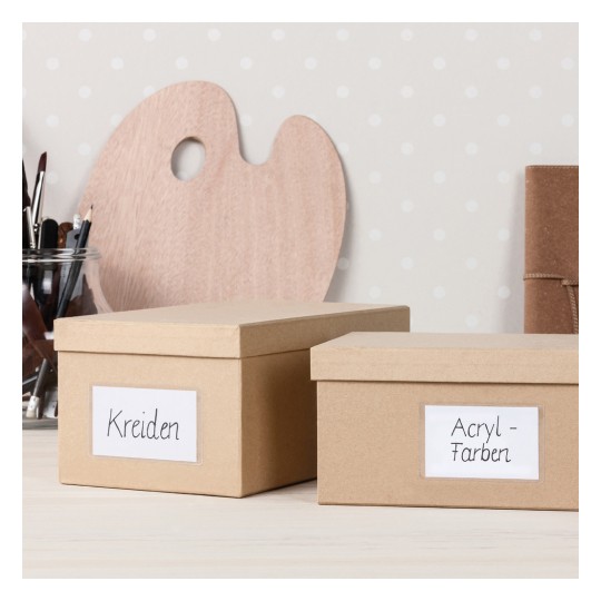 Imaginea arată două cutii etichetate pe un spațiu de lucru. O cutie este etichetată 'Kreiden' și cealaltă 'Acryl-Farben', cu o paletă de lemn și pensule în fundal.
