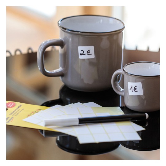 Imaginea arată două căni ceramice pe o suprafață neagră. Cana mai mare are un preț de 2€, iar cea mai mică de 1€. Lângă ele se află și foi de etichete și un pix negru.