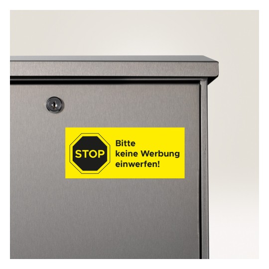 Imaginea arată un prim-plan al unei cutii poștale cu un autocolant galben strălucitor care spune 'STOP bitte keine Werbung einwerfen!', indicând că nu ar trebui să fie introduse materiale publicitare.