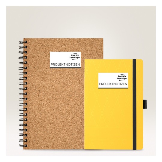 Imaginea prezintă două caiete: unul este legat cu spirală și are o copertă din plută, iar celălalt este un caiet galben cu copertă rigidă și o bandă elastică. Ambele au etichete pe care scrie 'PROJEKTNOTIZEN' și 'Avery Zweckform'.