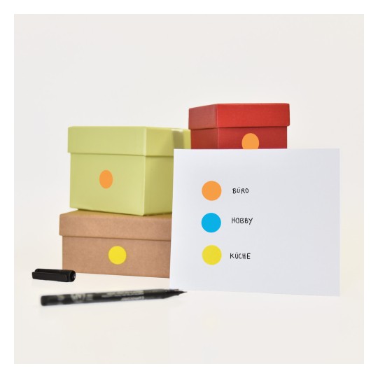 Imaginea arată mai multe cutii colorate stivuite una peste alta cu un card care are trei puncte etichetate: portocaliu pentru 'BÜRO', albastru pentru 'HOBBY' și galben pentru 'KÜCHE'. Un stilou negru este, de asemenea, vizibil lângă cutii.