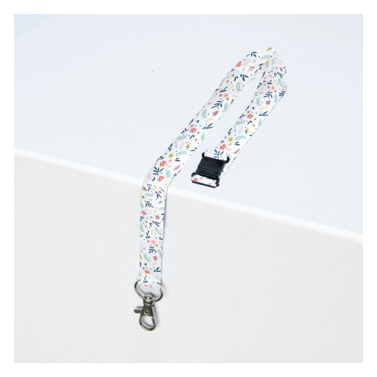 Imaginea arată un șnur cu modele florale și un clips metalic, așezat pe o suprafață deschisă la culoare.