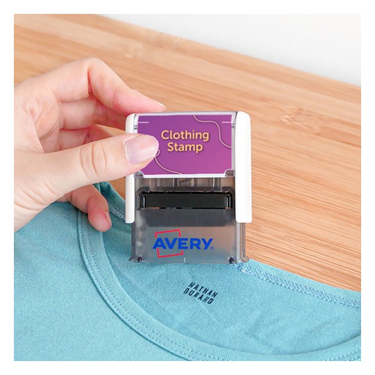 Imaginea arată o persoană ținând un ștampile pentru haine, poziționată deasupra unei cămăși. Ștampila este marcată cu 'Ștampilă pentru haine' și are vizibil numele brandului 'Avery'.