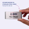 Imaginea afișează o mână ținând un ecuson de nume din oțel inoxidabil cu textul 'Avery Paul Meyer' pe el. Se menționează 20 de ecusoane disponibile cu finisaj din oțel inoxidabil, având dimensiunea de 70 x 30 mm.