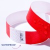 Imaginea arată o brățară roșie impermeabilă cu picături de apă pe ea. Există modele în zigzag și text pe o bandă albă a brățării.